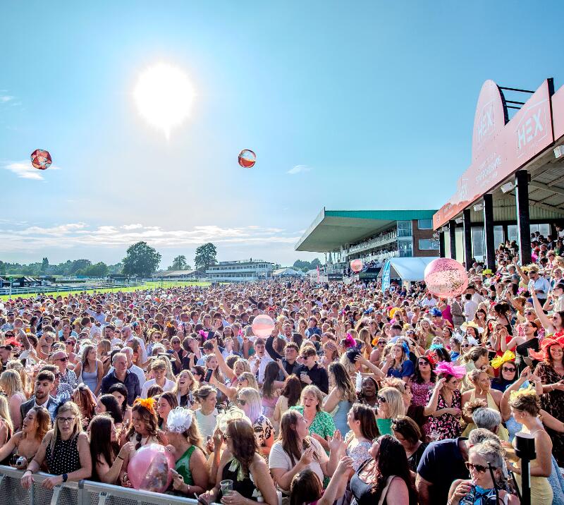A packed crowd in the sunshine at Uttoxeter Racecourse with beach balls in the air