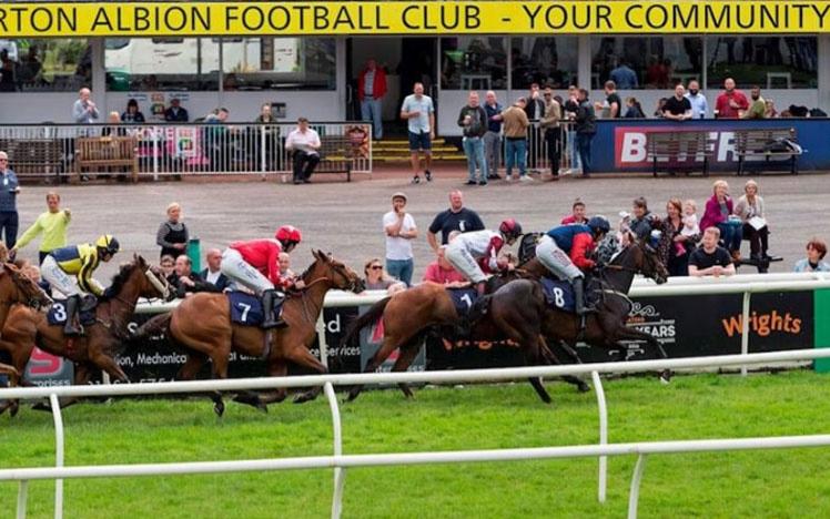 Group of jockeys racing past racegoers at Uttoxeter Racecourse.