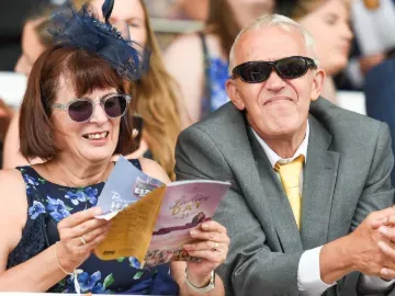 A well dressed couple at the races reading the racecard