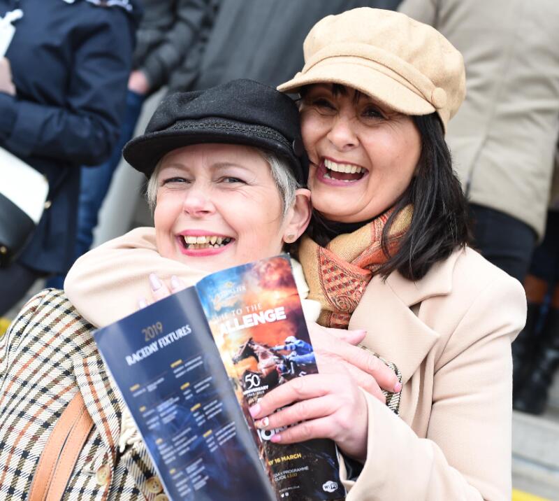 Visitors to Uttoxeter Races hug and laugh while holding a race card